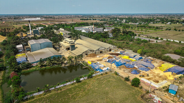 Aerial view of active rice mill with smokestack, paddy stockyard, processing buildings, and water pond in rural agricultural setting