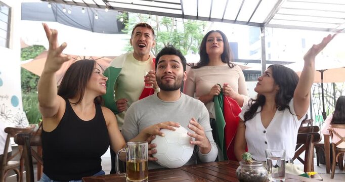 latin people soccer fans watching and cheering a match game with goal, victory or winning championship in a terrace pub. Group of mexicans friends holding a flag in celebration at bar together