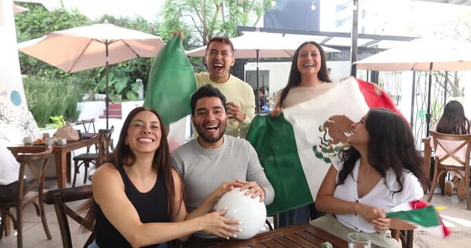 latin people soccer fans watching and cheering a match game with goal, victory or winning championship in a terrace pub. Group of mexicans friends holding a flag in celebration at bar together