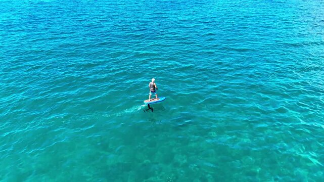 Aerial view of a person riding a hydrofoil board across the turquoise ocean water under the bright sun in Kawaihae, Hawaii, United States.