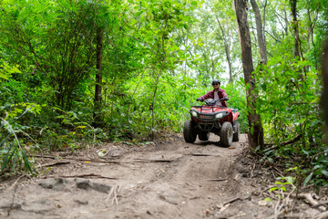 Fototapeta premium Riding an ATV on a dirt trail in the forest with trees and greenery around during the day