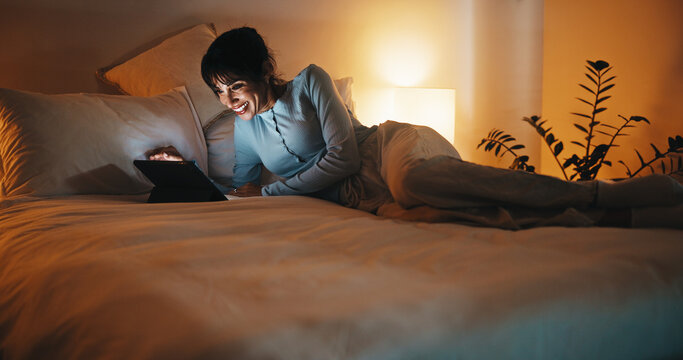 Bed, woman and streaming on tablet at night for binge watching series, funny episode or relax. Weekend, mature person or laugh with tech in home for comedy film, tv show subscription or entertainment