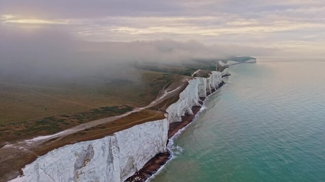 Aerial view of Seven Sisters Cliffs with white chalk cliffs and rolling green hills under a misty sky Exceat, England, United Kingdom.