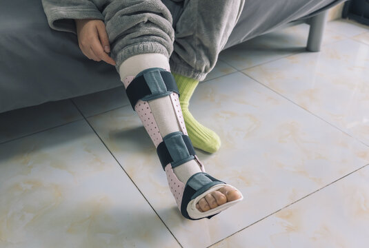 A person sits indoors, their lower leg secured in a pink and black medical splin