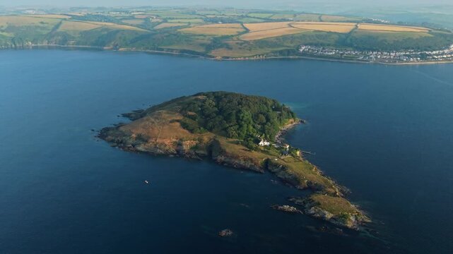 Aerial view of Saint Georges Island featuring lush green trees and rocky shores surrounded by the blue sea near the coast of Looe, England, United Kingdom.