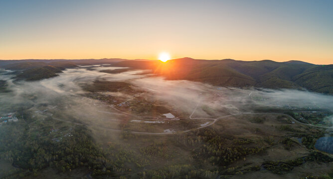Sunrise mist settling over a tranquil rural valley, revealing a winding river and green forests