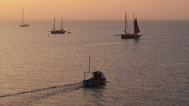 Aerial view of traditional fishing boats and sailboats drifting on the calm sea during a golden sunset in Looe, England, United Kingdom.