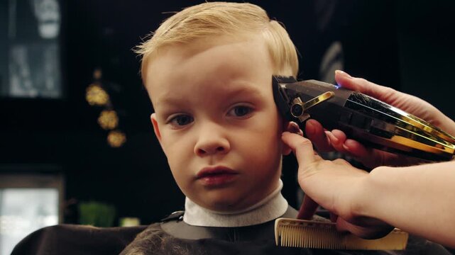 Stylist trimming a child in a stylish beauty salon with a buzzer.. Cinematic shot of a hairdresser working with a young client. Small local business.
