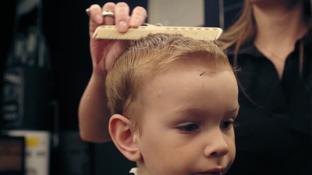 Professional female barber cutting a young boy's hair in a modern barbershop with scissors. Stylist trimming a child in a stylish beauty salon.