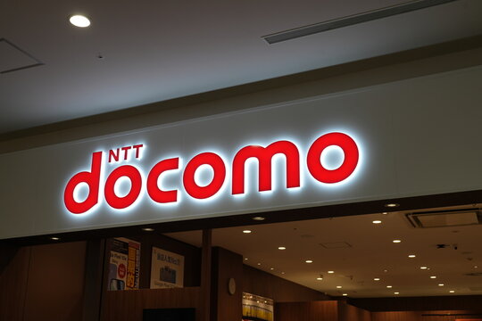 A glowing red NTT docomo logo sign at a store entrance in Japan.