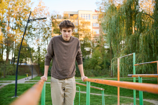 Teen boy training on parallel bars in city park, focused on upper body exercise in autumn light. For fitness, youth wellness, outdoor recreation, motivation, or lifestyle campaigns