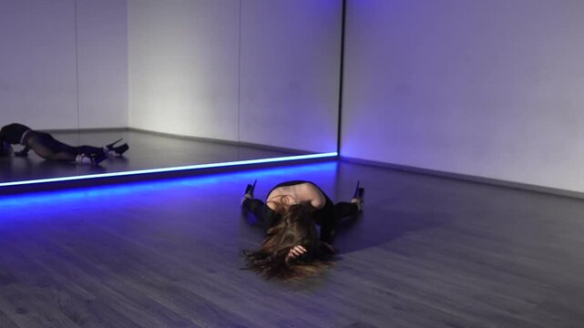 Dancer choreography floorwork young woman performs expressive sensual routine on wood floor in mirrored studio lighting.
