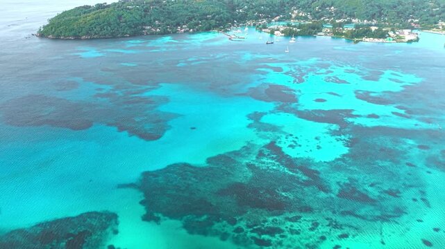 Aerial view of Praslin Ferry Harbour with turquoise waters and coral reefs along the lush tropical coastline of Baie Ste Anne, Baie Sainte Anne, Seychelles.