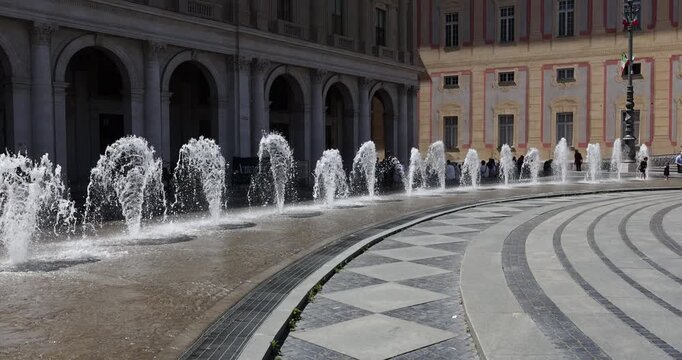 Fountain water jets splashing at Piazza De Ferrari in Genoa Italy. Historic architecture of Palazzo Ducale with ancient arches and sunny city square background. Mediterranean urban landscape captured