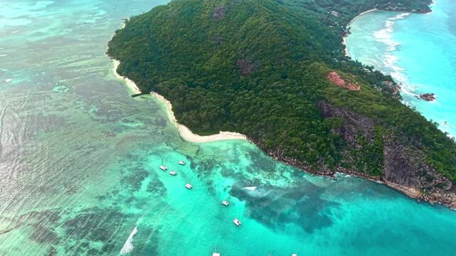 Aerial view of the lush green hills and white sandy beaches of Praslin island with boats anchored in turquoise waters, Praslin, Praslin, Seychelles.