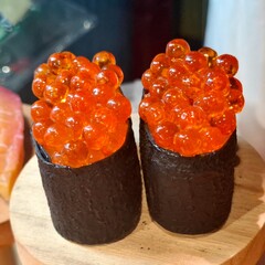 Two pieces of delicious ikura gunkan maki sushi topped with salmon roe wrapped in crispy nori seaweed on a wooden plate © Rungphailin