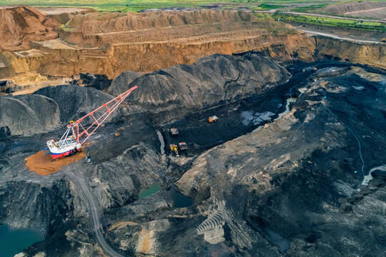 Aerial panoramic view captures industrial scale coal mining operation featuring large dragline excavator and multiple haul trucks