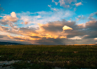 Obraz premium Expansive grassy field under a dramatically lit sky with golden clouds and distant mountains during evening