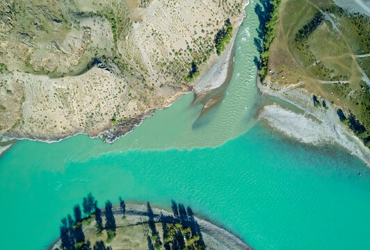 Aerial view shows Altai river confluence showing vibrant turquoise water merging with lighter green stream in a vast natural landscape