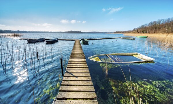 Clear sunny winter day at the Schaalsee, wooden jetty in the reeds with a rowing boat full of water, Schaalsee Biosphere Reserve, Mecklenburg-Western Pomerania, Germany