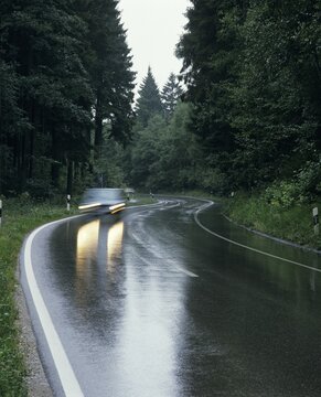 Car with lights driving through curves of a wet coutnry road in the rain Upper Bavaria Germany
