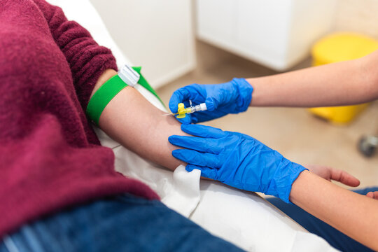 Blood draw procedure in hospital laboratory. Close-up of nurse inserting needle into arm vein of patient with green tourniquet. Healthcare and medicine, medical test, blood donation concept.