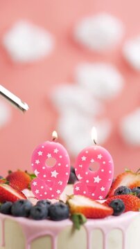 Birthday cake candle number 99. Vertical video of candle and cake on pink background and fire by lighter. Close-up and slow motion