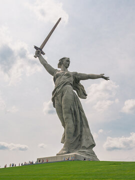 Volgograd, Russia - August 04, 2021: Giant Motherland Calls monument on Mamayev Kurgan overlooks green grass where numerous visitors gather.