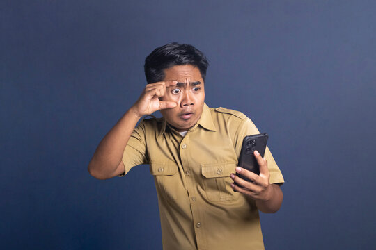 Indonesian civil servant widening eye with fingers in shock while looking at smartphone screen