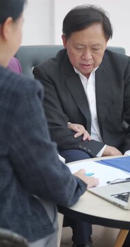 Senior Asian couple listening to a financial advisor or real estate agent presenting on a laptop.