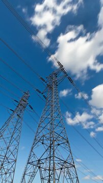Electrical transmission towers with power lines against blue cloudy sky, vertical footage