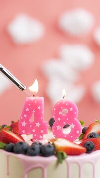 Birthday cake candle number 48. Vertical video of candle and cake on pink background and fire by lighter. Close-up and slow motion