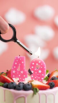 Birthday cake candle number 49. Vertical video of candle and cake on pink background and fire by lighter. Close-up and slow motion