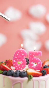 Birthday cake candle number 65. Vertical video of candle and cake on pink background and fire by lighter. Close-up and slow motion