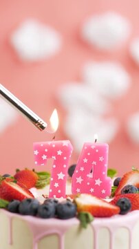 Birthday cake candle number 74. Vertical video of candle and cake on pink background and fire by lighter. Close-up and slow motion