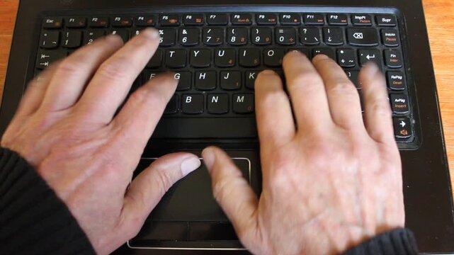Videoclips de las manos de un hombre escribiendo en el teclado en una computadora port&aacute;til sobre una mesa de madera. La imagen transmite trabajo, tecnolog&iacute;a y productividad, remoto en casa.