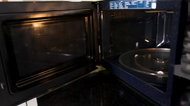 Person Opening Microwave Door and Placing Popcorn Bag Inside Kitchen Appliance