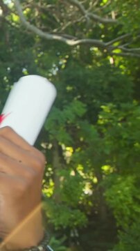 Vertical video: Entering hand in blue sleeve offering scroll in park, showing red ribbon and watch