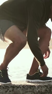 Vertical video: Stepping hoodie runner squatting tying laces on bay ledge before run with earphones