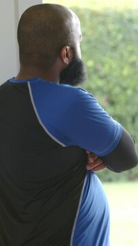 Vertical video: Standing man, shaved head and beard, watching yard at porch, wearing blue shirt