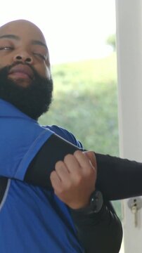 Vertical video: Pulling right arm across chest, man in blue tee by door, warming up with smartwatch