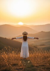 Fototapeta premium Young Woman in White Dress with Outstretched Arms Enjoying the Sunset Over Mountain Valley Landscape