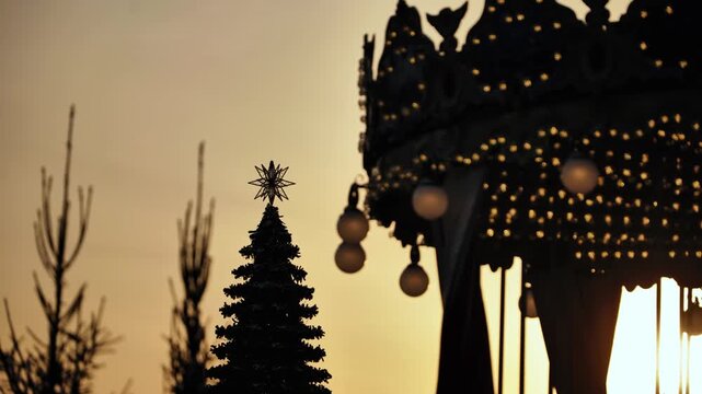 Christmas tree star and carousel canopy silhouette against a golden winter sunset