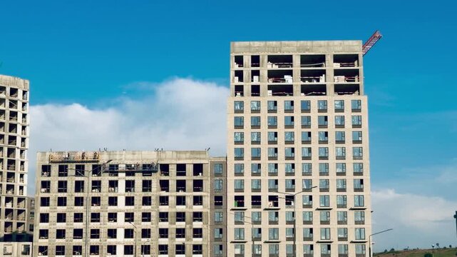 Unfinished high rise multi story houses under construction in Moscow, Salaryevo Park block development project by PIK group, concrete housing estate buildings facade against bright blue sky.