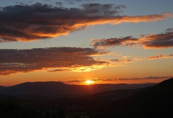 Fototapeta premium Vibrant Orange Sunset and Dramatic Clouds Setting Behind Mountain Range