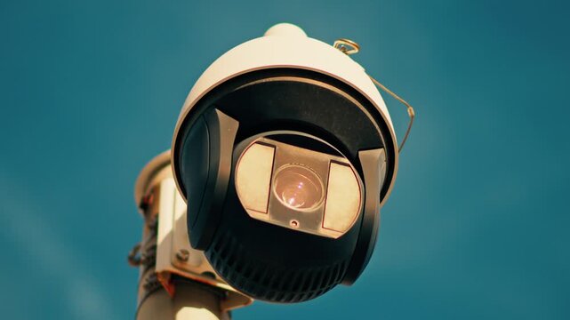 Close up of security camera with blue sky background, surveillance technology in motion.