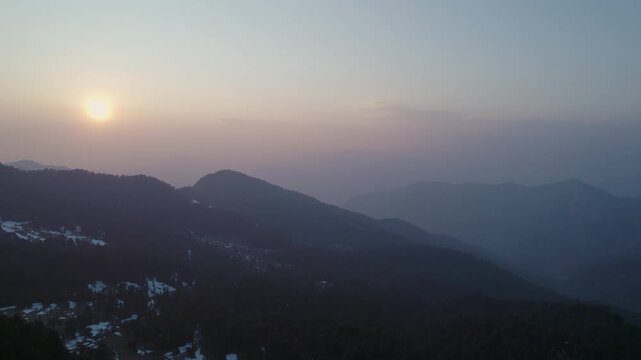 Aerial view of Chopta Tungnath with snow-capped mountain ridges and hazy sunset sky in Chopta, Uttarakhand, India.
