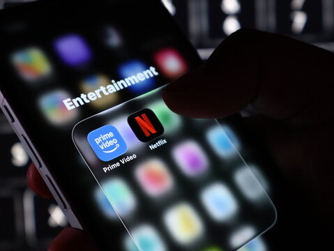 Closeup of a person holding a smartphone displaying an entertainment folder with prime video and netflix app icons on the screen