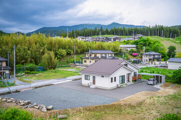 新緑の山あいに整備された新築の戸建て一軒家。地方で新しい生活を始める住宅地の風景。 / A newly built modern detached house in a rural residential area surrounded by green mountains. © Kimikatsu