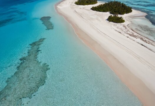 Aerial view of a long white sandbar stretching through emerald green ocean